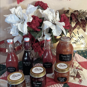 photo of a Christmas display of jarred products, including apple butter, Christmas jam, carrot cake jam, strawberry syrup, blueberry syrup, raspberry syrup, and apple pie filling.