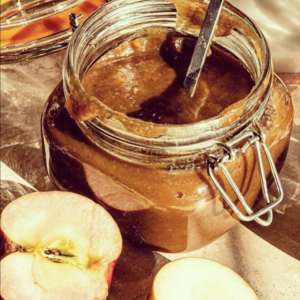 photo of an open jar of apple butter with cut apples around it