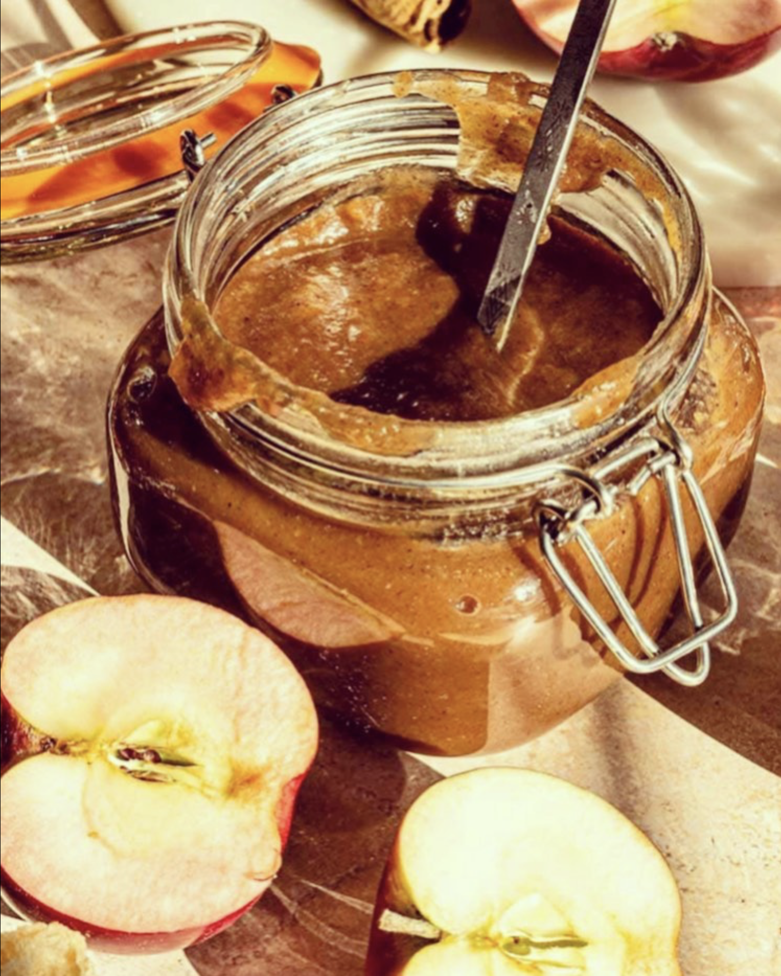 photo of an open jar of apple butter with cut apples around it