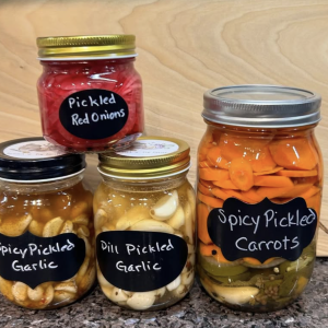 a photo of four jars of pickled vegetables on a counter: dill pickled garlic, spicy pickled garlic, spicy pickled carrots, and pickled red onions