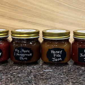 photo of four jars of products from the farm: fig strawberry jam, fig apple and pomegranate jam, honey fig jam, and fig jalapeño jam.