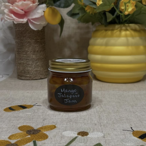 a photo of a jar of mango jalapeño jam in front two flower pots