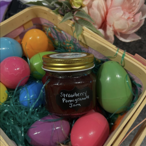 Photo of a jar of strawberry pomegranate jam in an easter basket filled with colorful easter eggs on a bed of green grass
