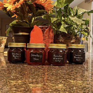 Photo of four products in jars: strawberry blueberry jam, strawberry jam, rosella hibiscus jelly, and lemon blueberry jam