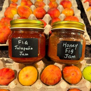 a photo of two jars, fig and jalapeño jam and fig and honey jam, sitting on a carton of figs freshly picked from the farm.